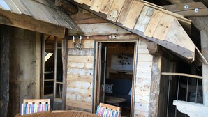 Une cabane en bois avec une table et des chaises rondes en bois, un espace de couchage en mezzanine et un aménagement intérieur rustique.