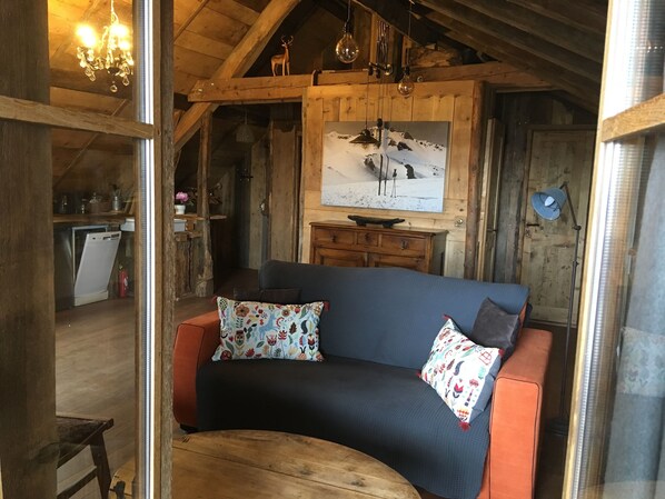 L’intérieur chaleureux d’un chalet avec un canapé incurvé, des murs en bois, une tête de cerf accrochée au mur et un tableau représentant un paysage enneigé.