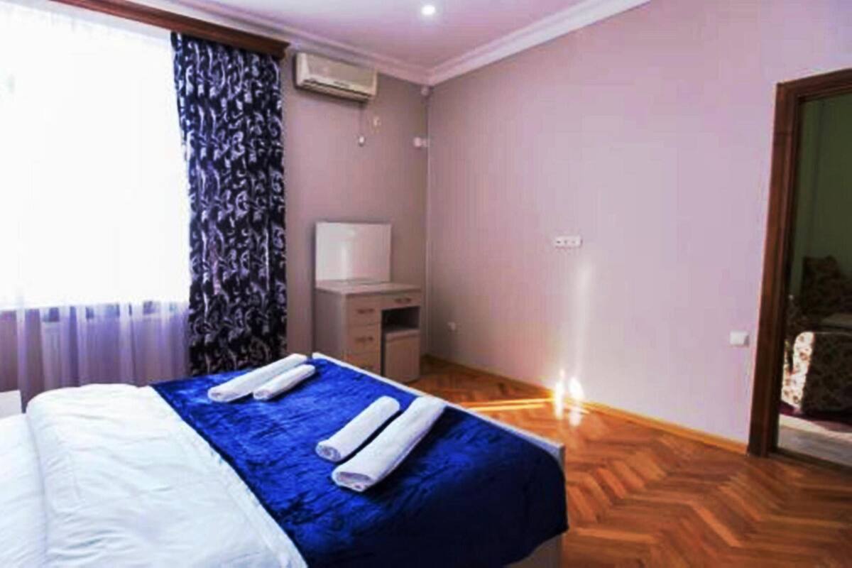 A hotel room with a bed, a desk, an air conditioner, and a window with curtains.