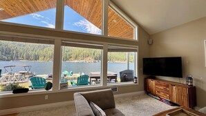 A living room with a large window overlooking a lake, a television, and a wooden entertainment center.