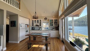 A spacious kitchen with wooden flooring, white cabinetry, and a large window overlooking a lake.