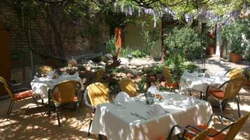 Un espace de restauration en plein air avec des tables pour deux, entouré de plantes et d’un mur en briques.