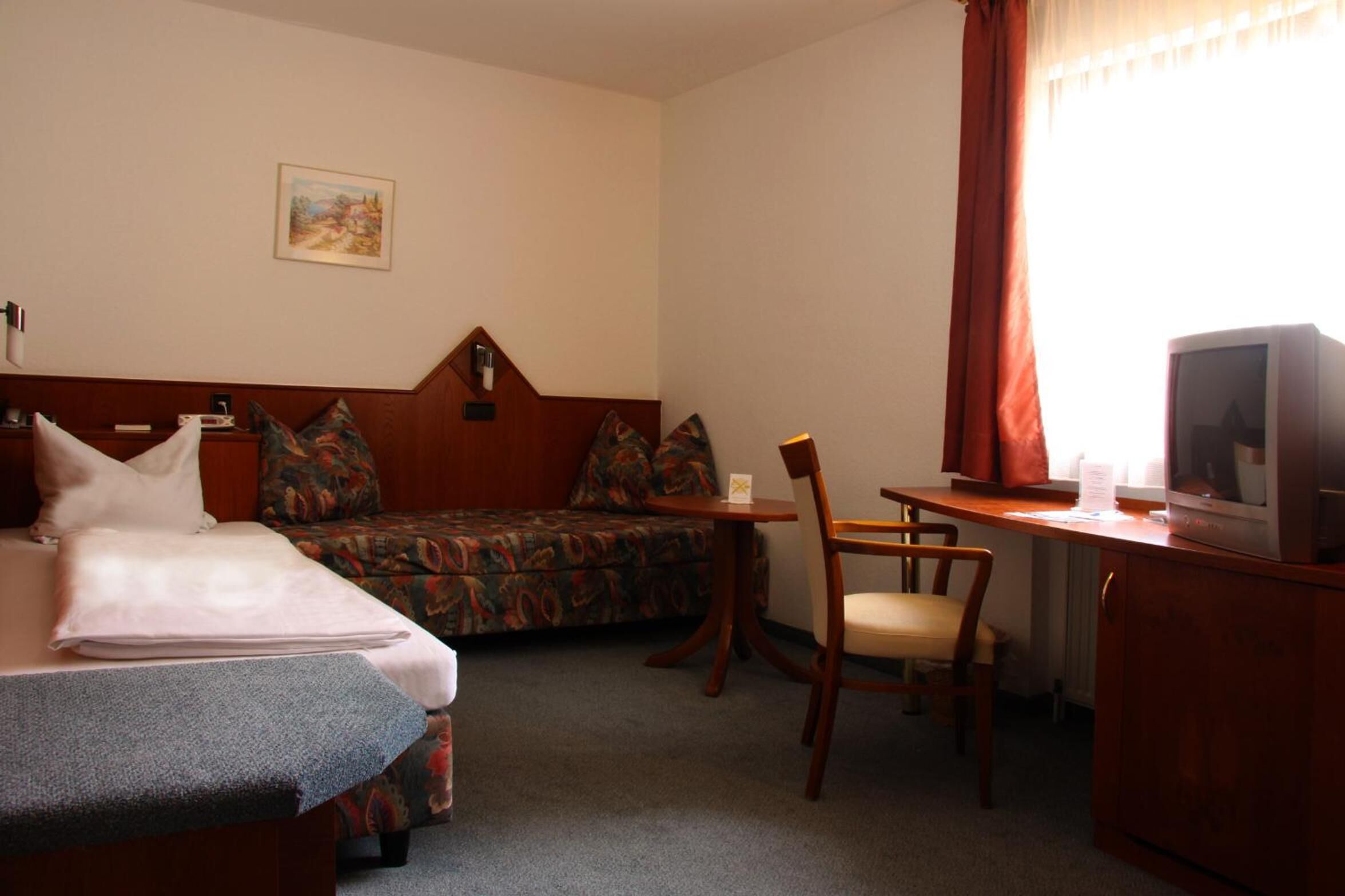 A hotel room with a bed, a sofa, a desk with a chair, and a television.