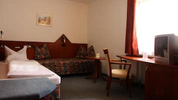 Et hotelværelse med seng, sofa, skrivebord med stol og fjernsyn.