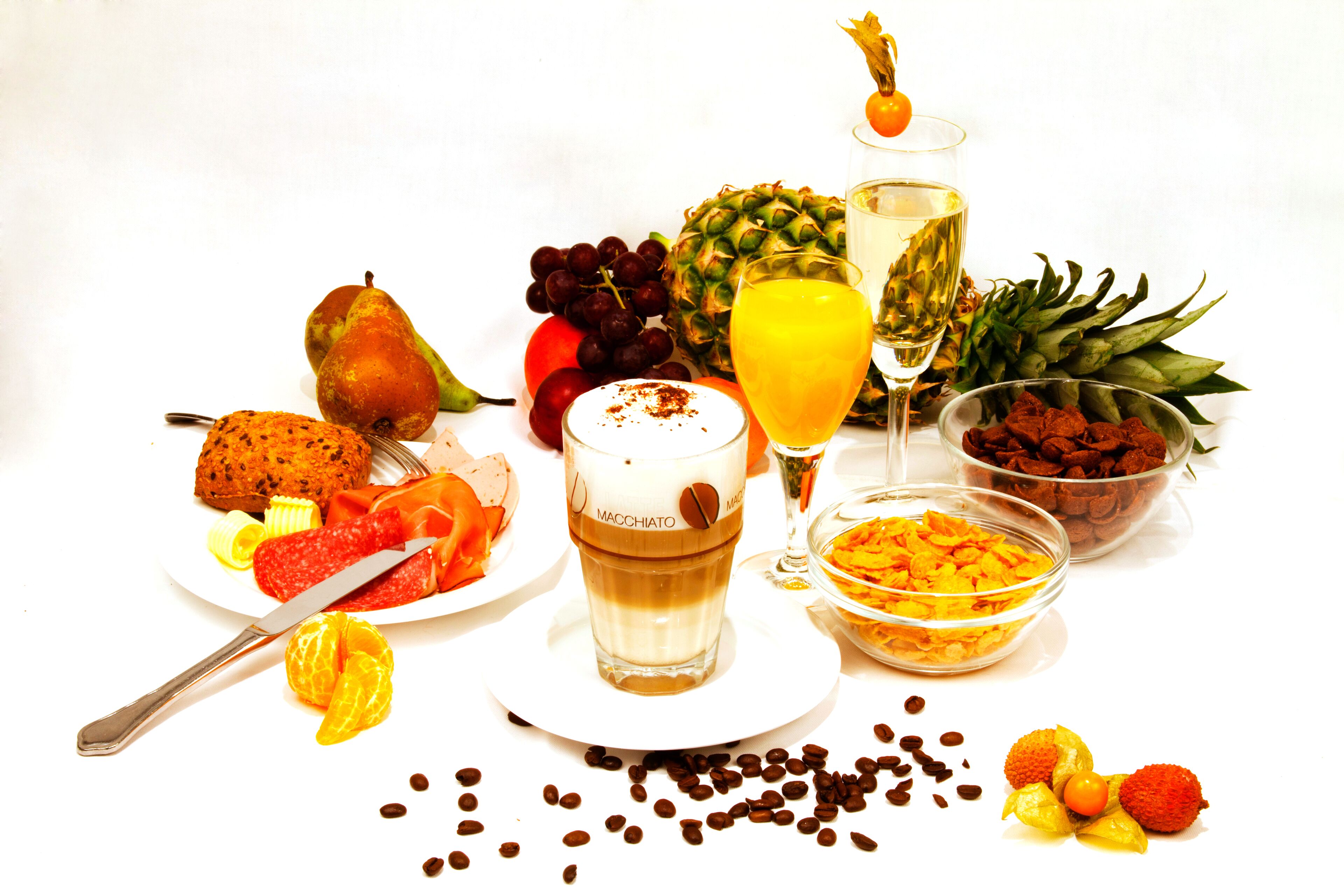 Ein Frühstückstisch mit verschiedenen Früchten, einem Glas Saft, Kaffee und einer Schüssel Müsli.