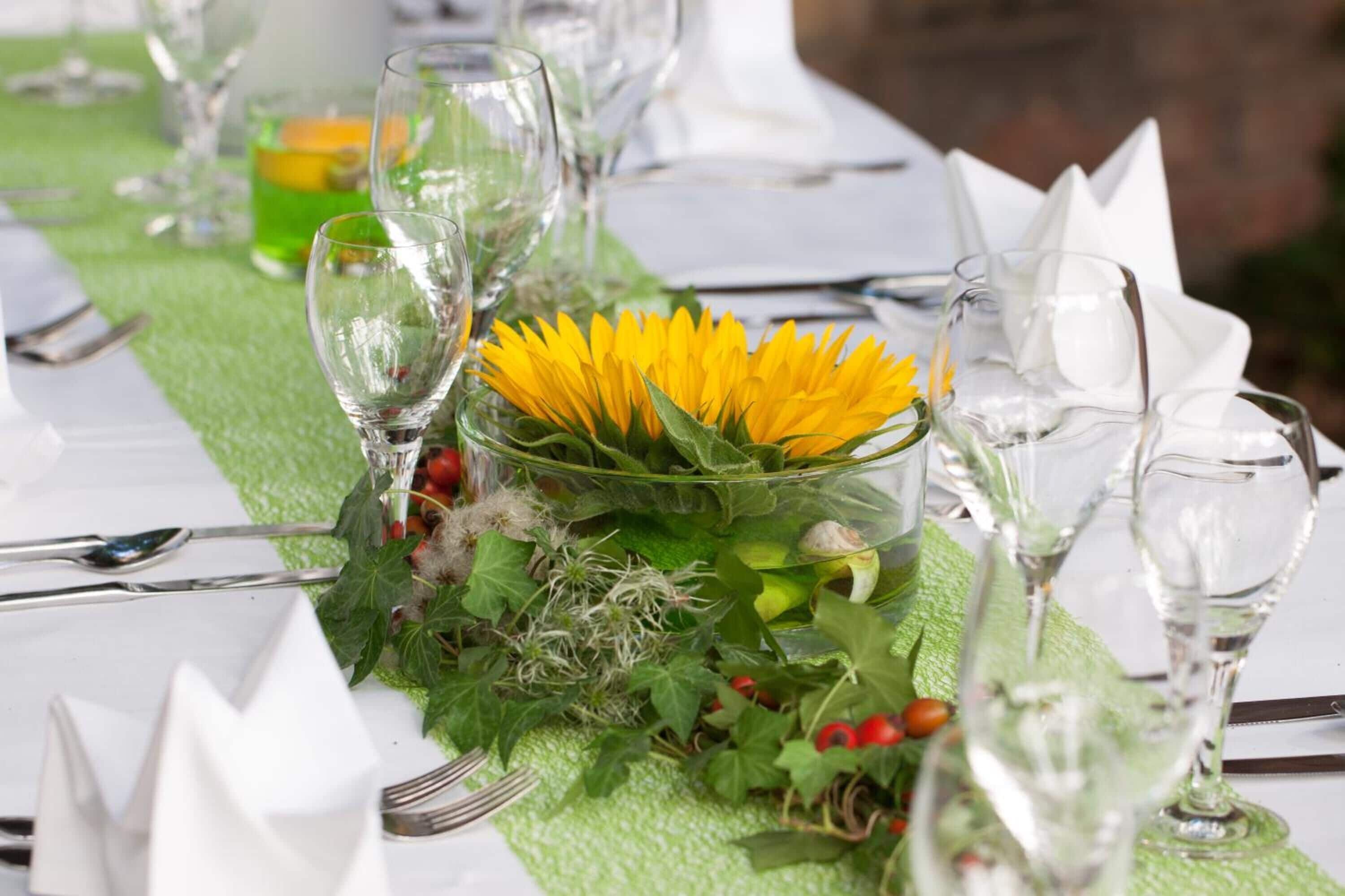 A table set with clear glassware, white napkins, and a centerpiece of yellow flowers and greenery.