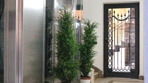 A modern hallway with a glass elevator, potted plants, and a black gate. - B&B Cloud (Santa Maria Capua Vetere)