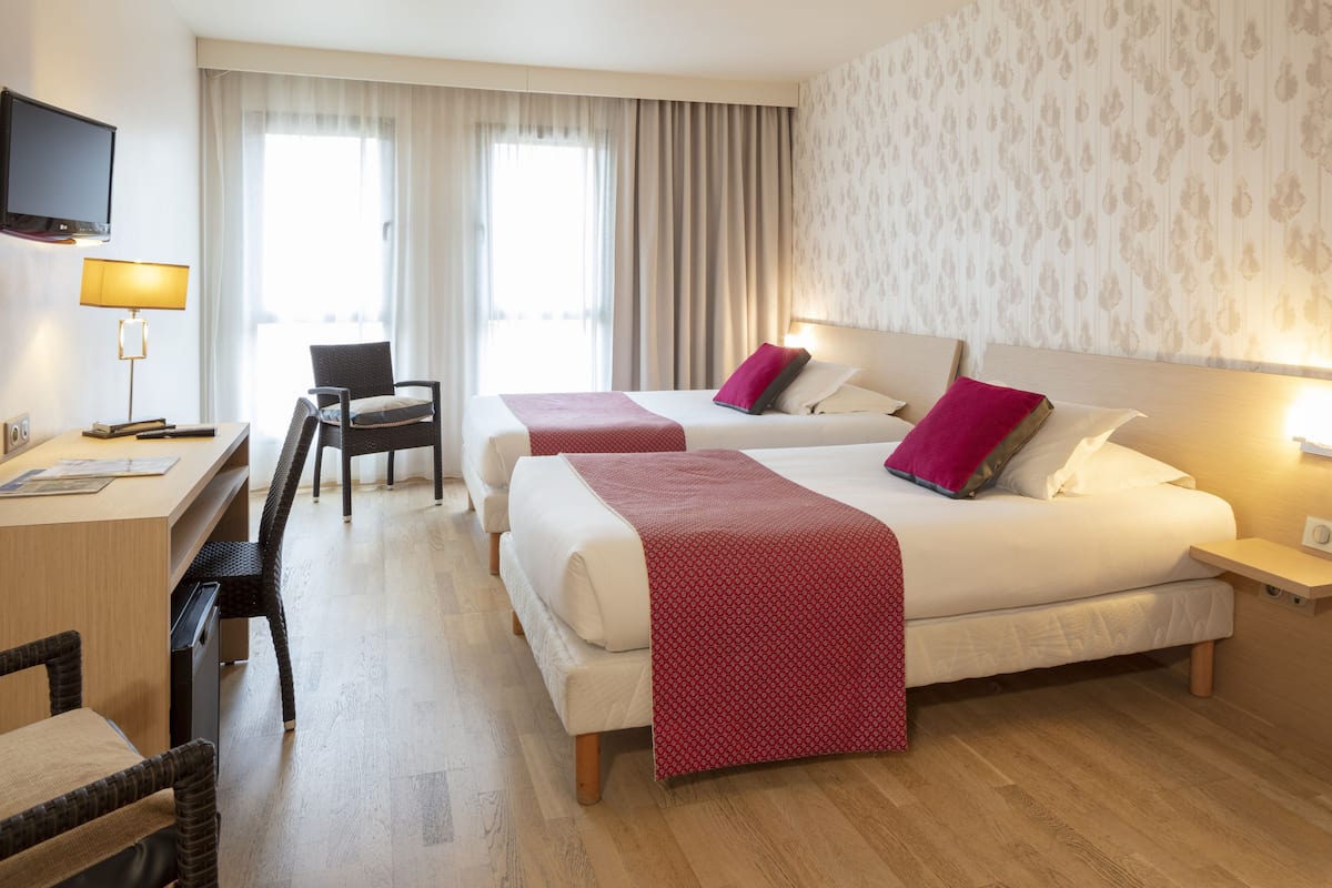 Ein Hotelzimmer mit zwei Betten, einem Schreibtisch, einem Stuhl, einem Fernseher und einem Fenster mit Vorhängen.