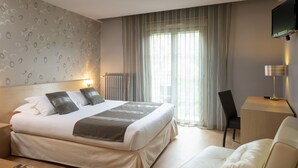 A modern hotel room with a large bed, a desk, a chair, and a TV mounted on the wall. - Hotel La Chaumiere (Quillan)