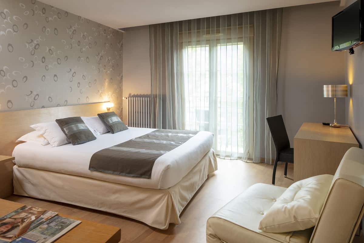 Ein modernes Hotelzimmer mit einem großen Bett, einem Schreibtisch, einem Sessel und einem an der Wand befestigten Fernseher.