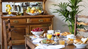 A breakfast table with various food items, a fruit bowl, and a mirror above it. - Hotel La Chaumiere (Quillan)