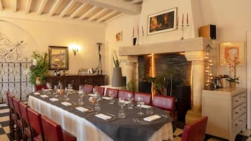 Un coin repas avec une longue table dressée pour un repas, entourée de chaises rouges, avec une cheminée et des appliques murales décoratives en arrière-plan.