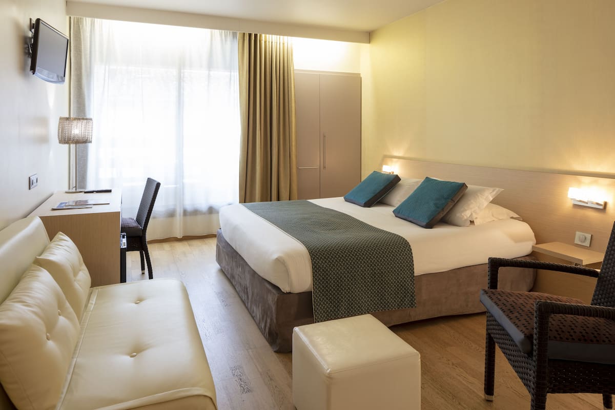 Ein Hotelzimmer mit Bett, Schreibtisch, Stuhl, Sofa und Fernseher.