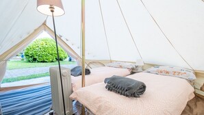 Ett tält med två sängar, en lampa och utsikt över grönskan utanför.