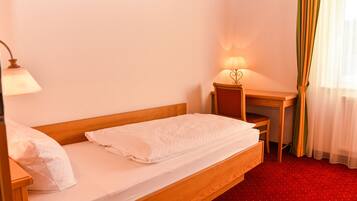 A single bed with a wooden frame, a nightstand with a lamp, and a small desk with a chair.
