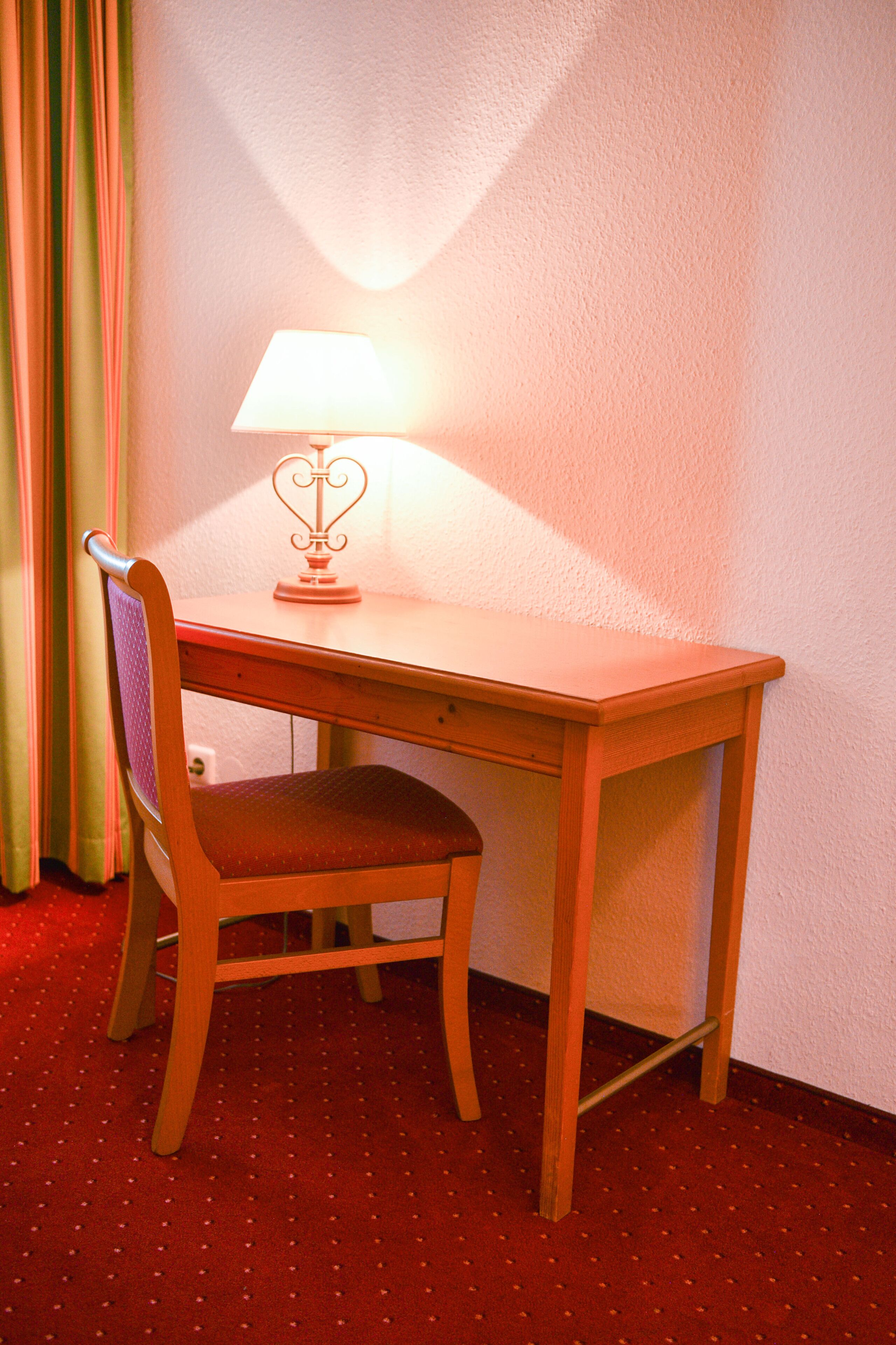 A corner desk with a chair, a lamp, and a red carpeted floor.
