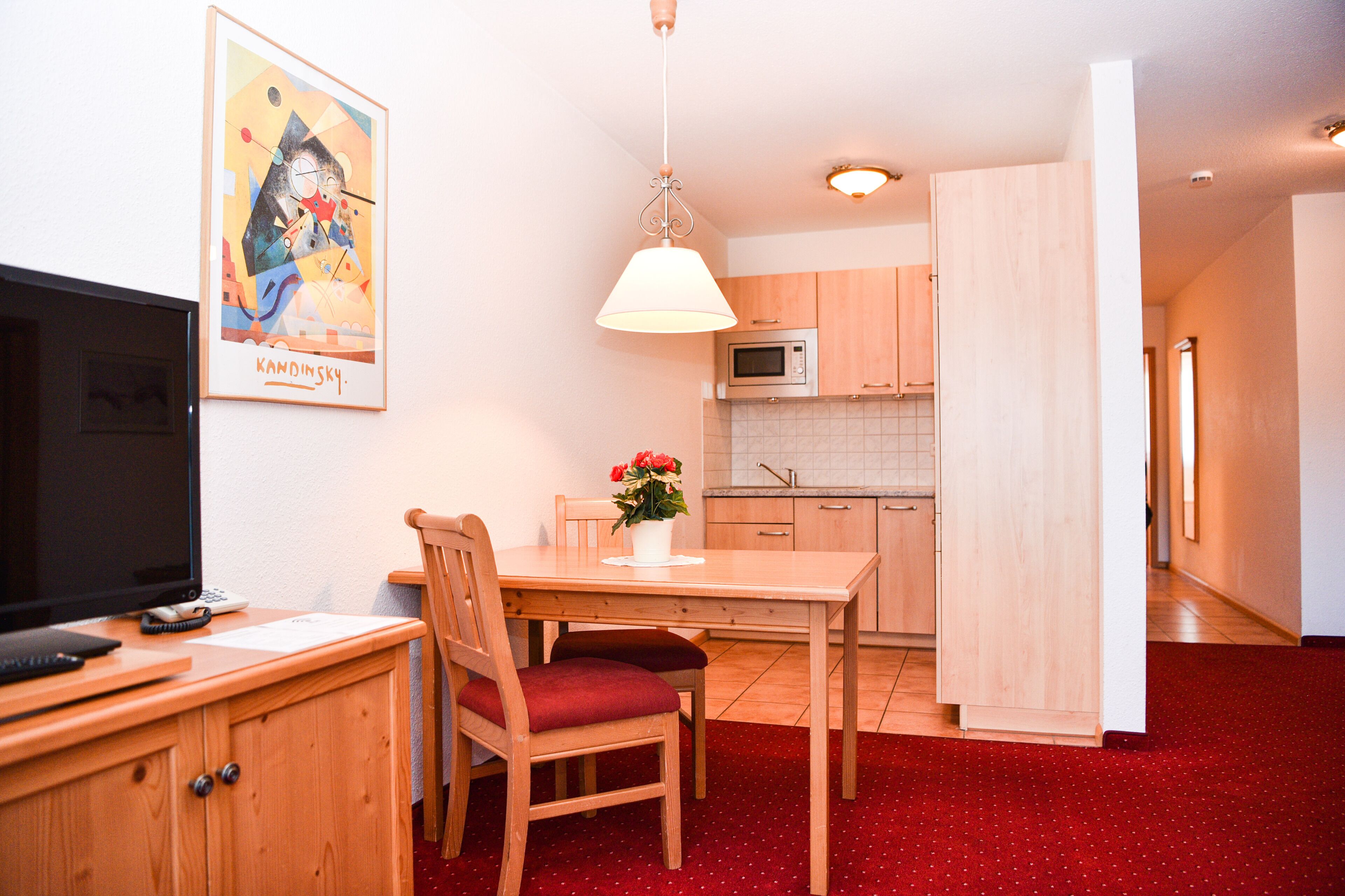 A compact living space with a dining area, kitchenette, and a television on a wooden cabinet.