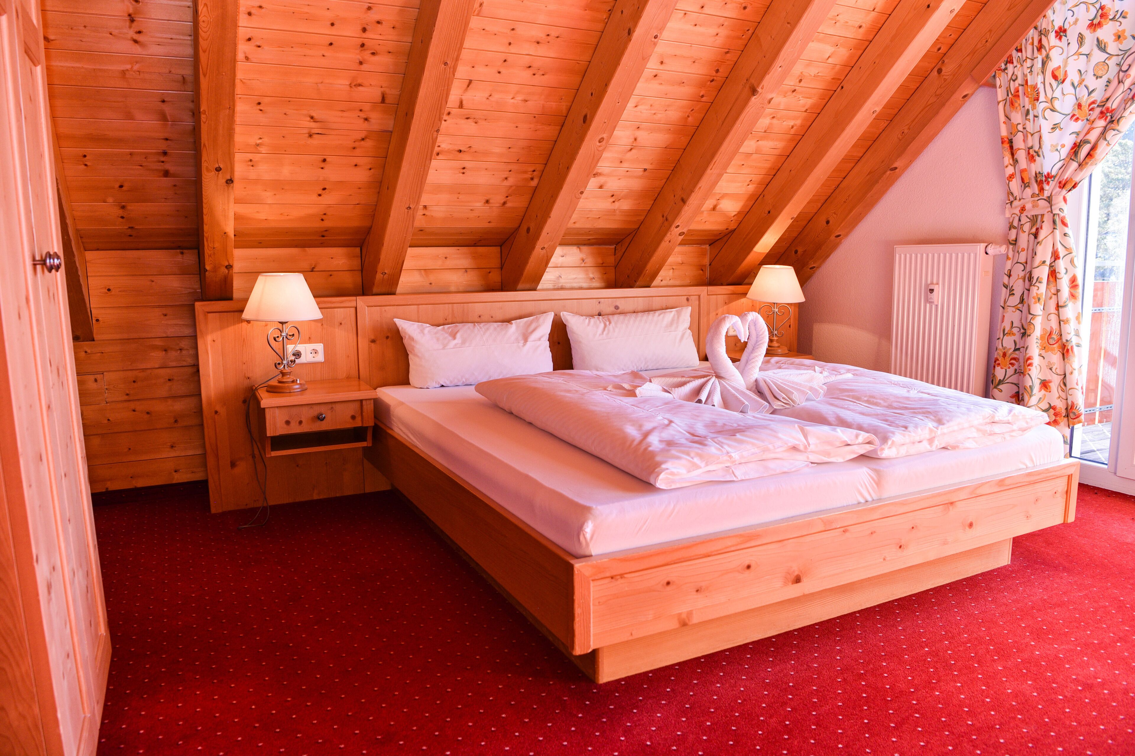 Un dormitorio de madera con cama, mesitas de noche y ventana con cortinas.