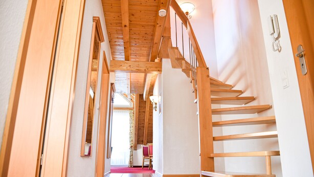 A wooden staircase with a handrail, leading to a landing with a door and a phone. - Aparthotel Sonnenburg (Schluchsee)
