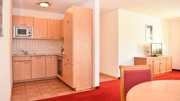 A compact kitchen with wooden cabinets, a microwave, and a red carpeted floor.
