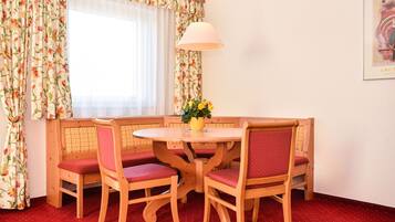 Un coin repas avec une table ronde en bois, quatre chaises dotées de coussins rouges, un vase avec des fleurs et une lampe suspendue.