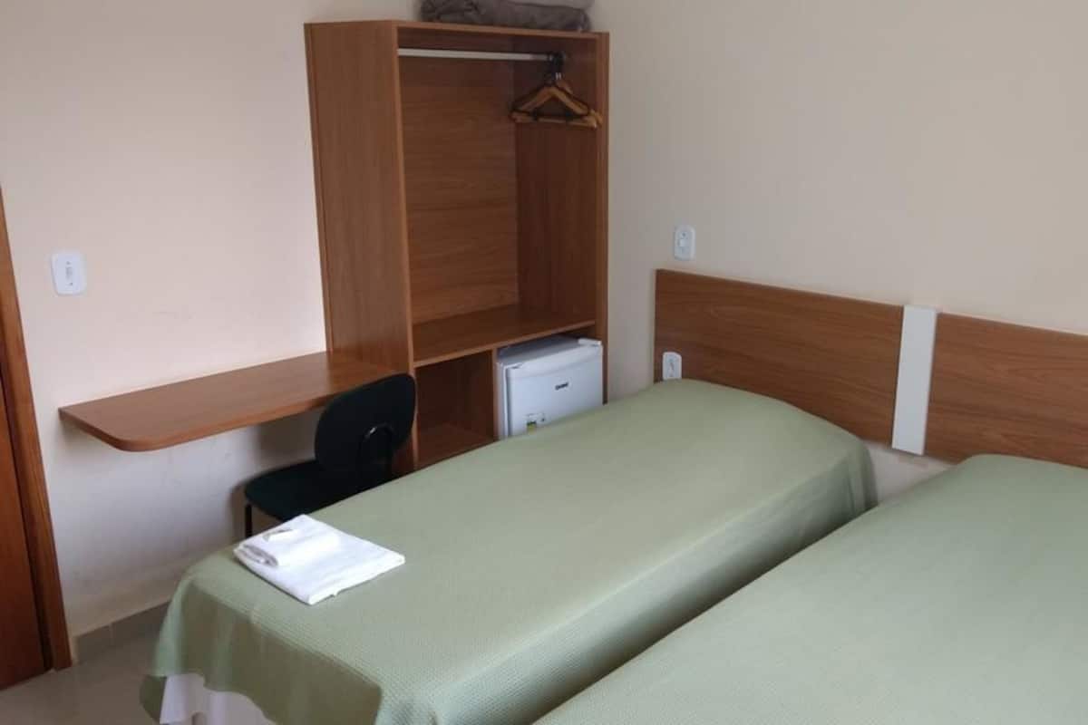 A room with two single beds, a wooden wardrobe, a desk, and a chair.