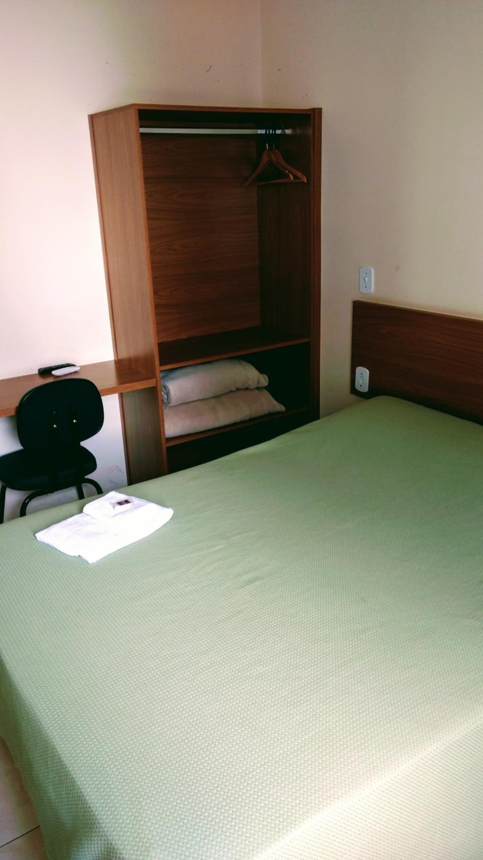 Une petite pièce comprenant un lit simple, une armoire en bois, une chaise et un bureau.