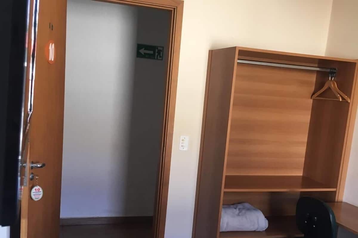 A hotel room with a bed, a wooden wardrobe, a desk, and a chair.