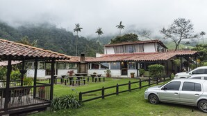 A white building with a red-tiled roof, surrounded by a wooden fence, and a parked car in front.