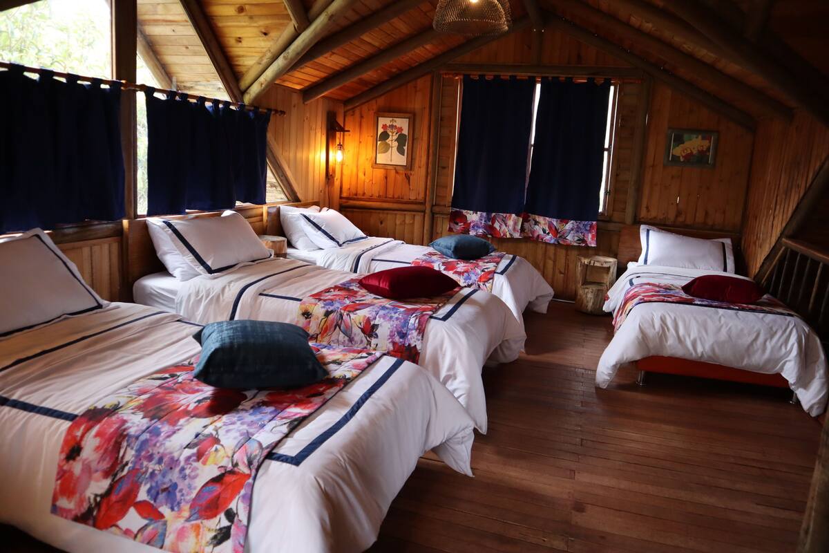 Una habitación tipo cabaña con tres camas, piso de madera y techo inclinado.