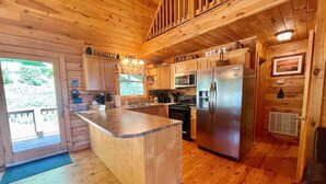 A wooden cabin kitchen with a central island, stainless steel appliances, and a cozy ambiance. - Sunrise Sensation - Great Views, Hot Tub, Gameroom, Close to Town, WIFI, Covered Porch (West Jefferson)