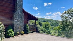 A log cabin with a stone chimney, a porch, and a view of a forested mountain. - Sunrise Sensation - Great Views, Hot Tub, Gameroom, Close to Town, WIFI, Covered Porch (West Jefferson)