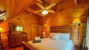 A wooden cabin bedroom with a bed, nightstands, a dresser, and a ceiling fan. - Sunrise Sensation - Great Views, Hot Tub, Gameroom, Close to Town, WIFI, Covered Porch (West Jefferson)