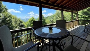 A covered outdoor deck with a round table and chairs, overlooking a mountainous landscape. - Sunrise Sensation - Great Views, Hot Tub, Gameroom, Close to Town, WIFI, Covered Porch (West Jefferson)
