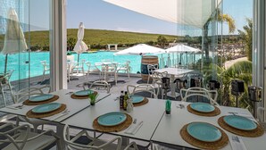 Ein Essbereich mit vier gedeckten Tischen, mit Blick auf einen Pool und eine Hügelkuppe.