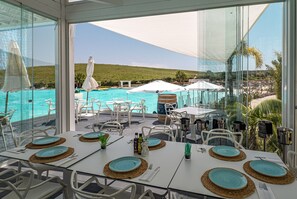 Un espace repas avec des tables disposées pour accueillir quatre personnes, offrant une vue sur une piscine et un paysage vallonné.