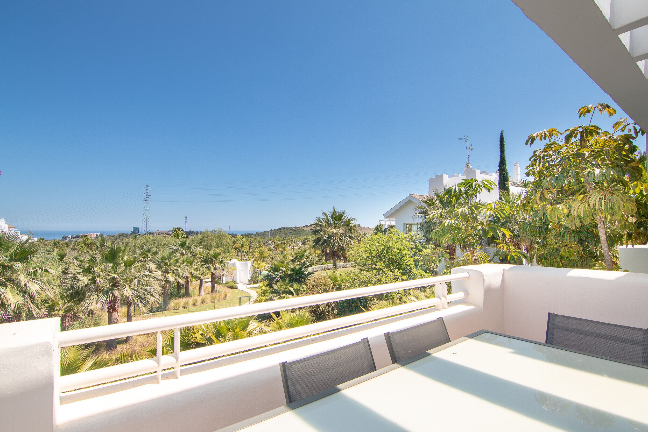 Un balcon doté d’une table et de chaises en verre, offrant une vue sur un jardin luxuriant et sur la côte.