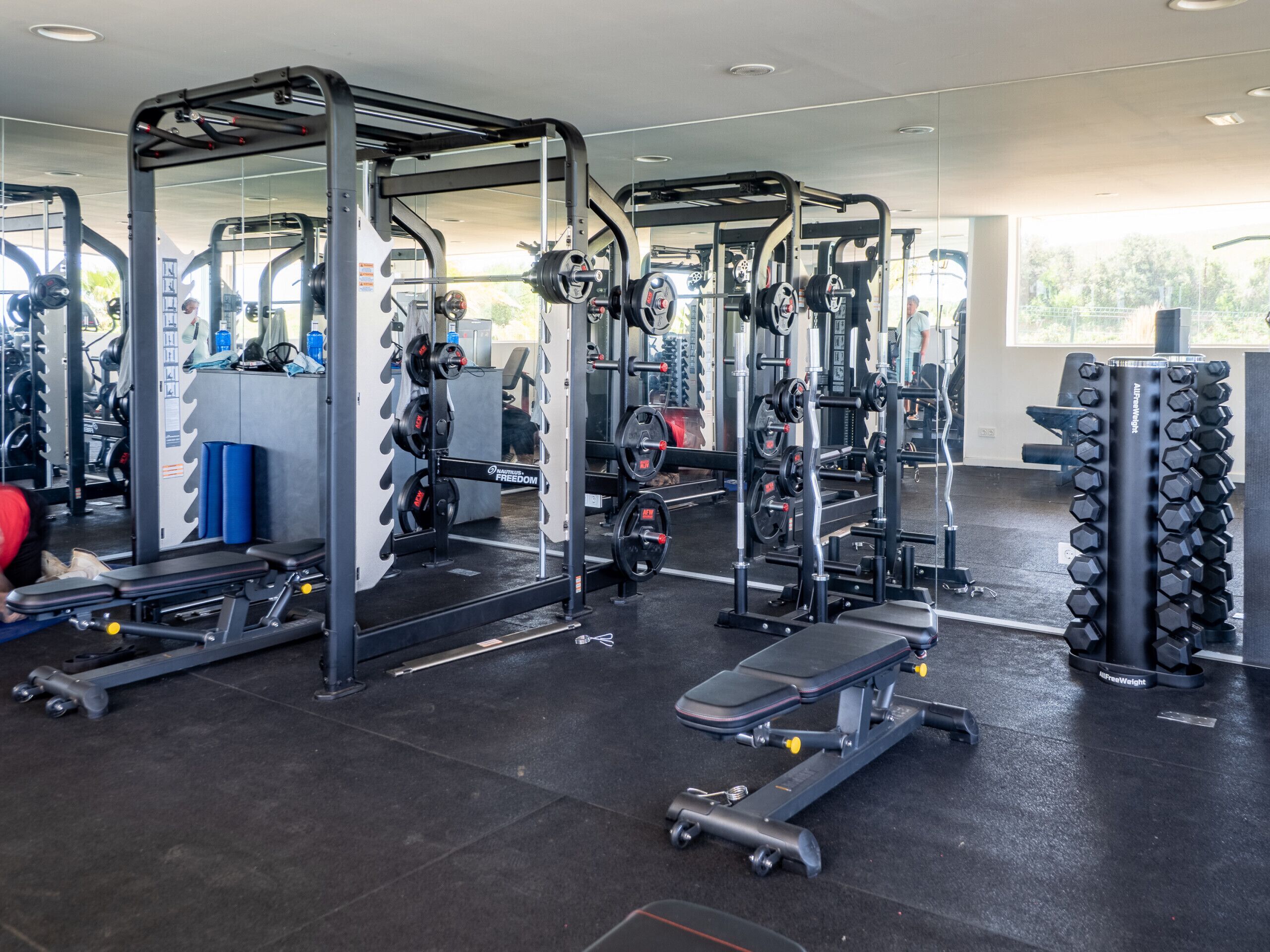 A gym with various weightlifting equipment, benches, and mirrors.