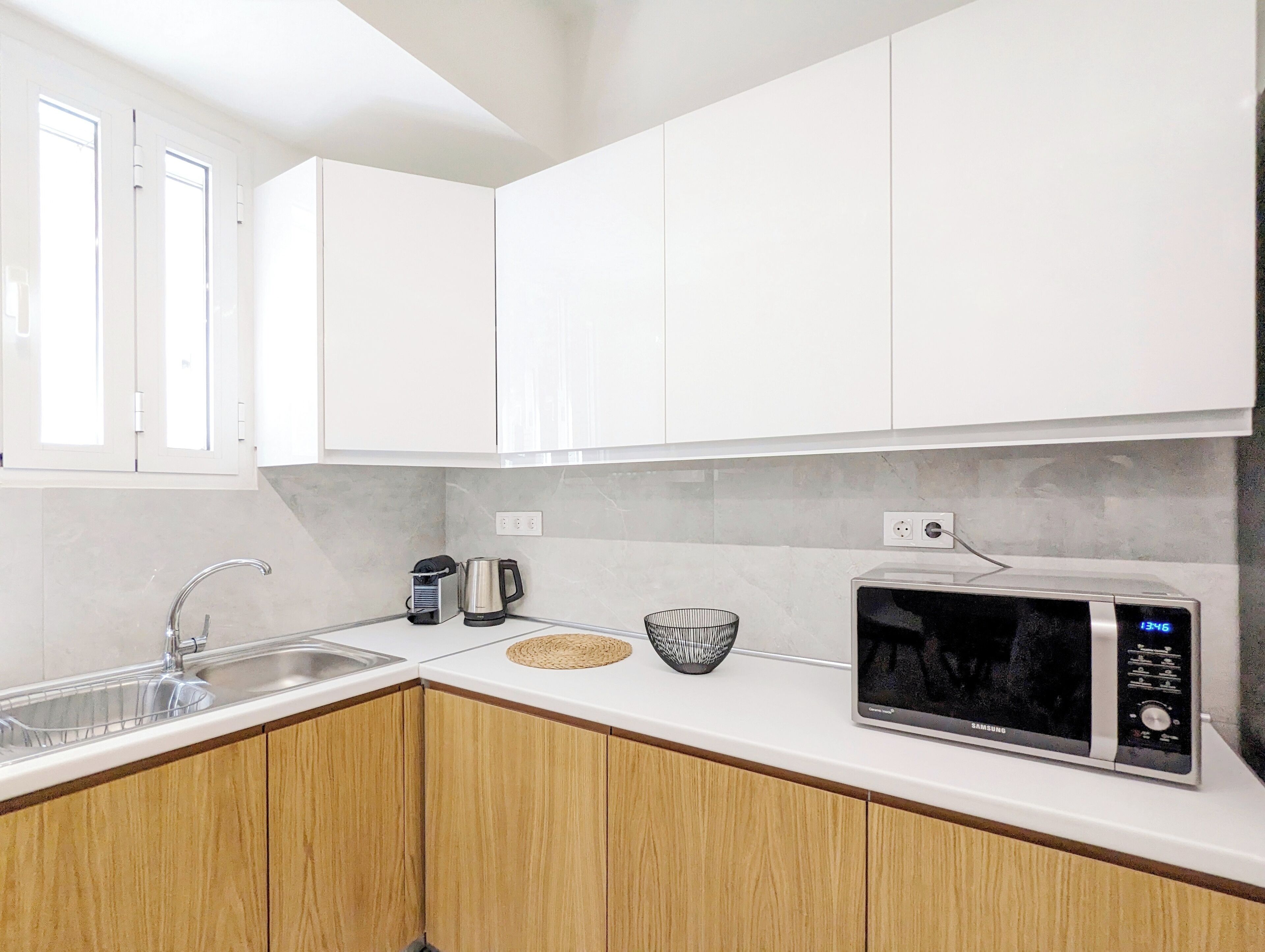 A modern kitchen with white cabinets, a stainless steel sink, a microwave, and a kettle.