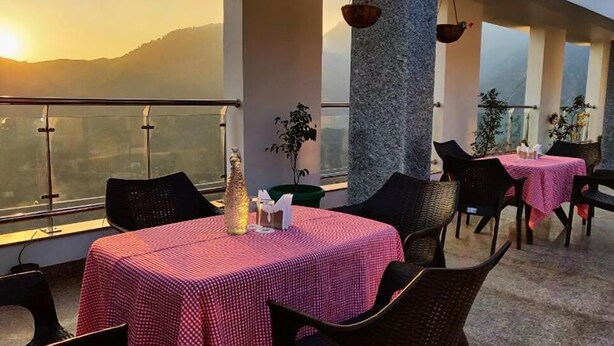 A restaurant with outdoor seating, tables covered with checkered tablecloths, and a view of mountains in the background. - Villa Bianca (Nainital)