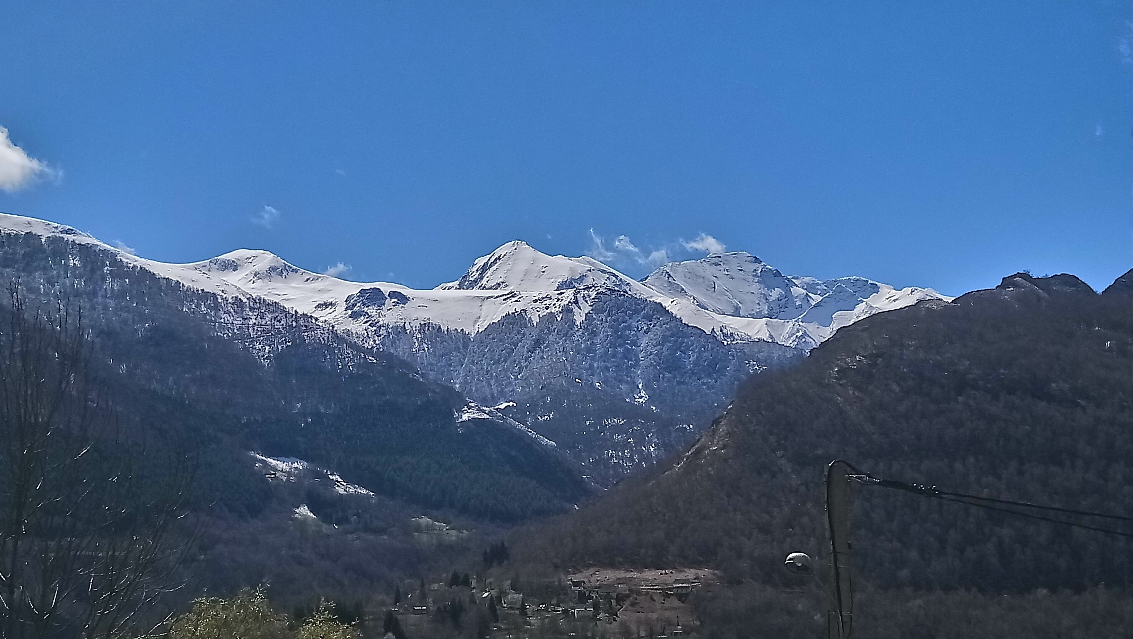 Un paysage montagneux aux sommets enneigés, un ciel d’un bleu limpide et une vallée à la végétation clairsemée.