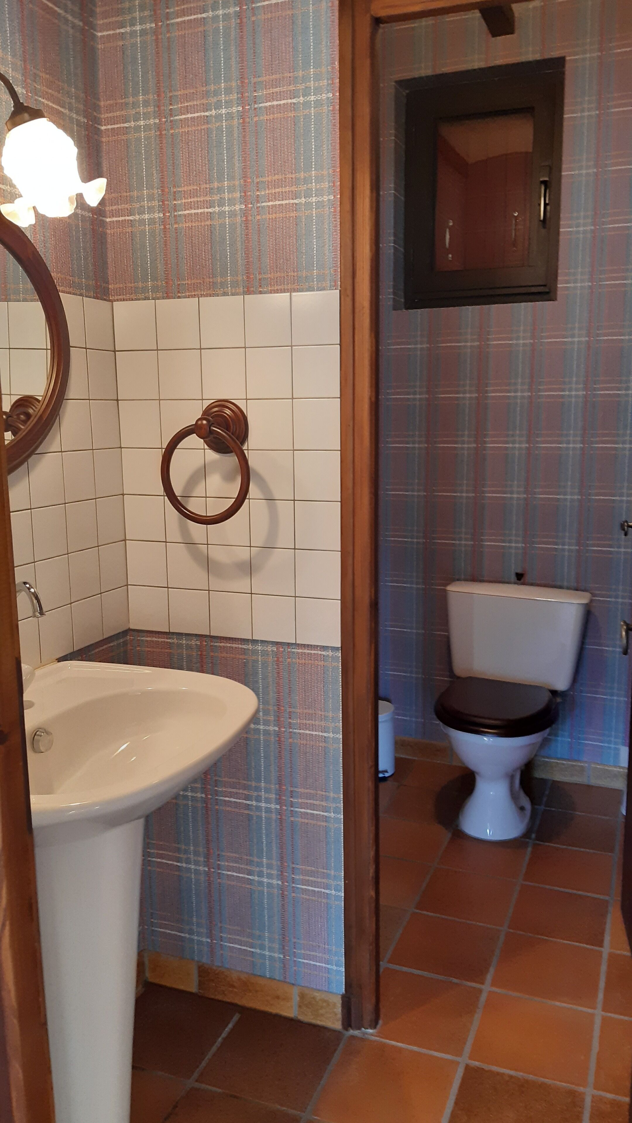A bathroom with a white sink, a toilet, and a mirror. The walls are tiled with a plaid pattern, and there is a wooden door frame.