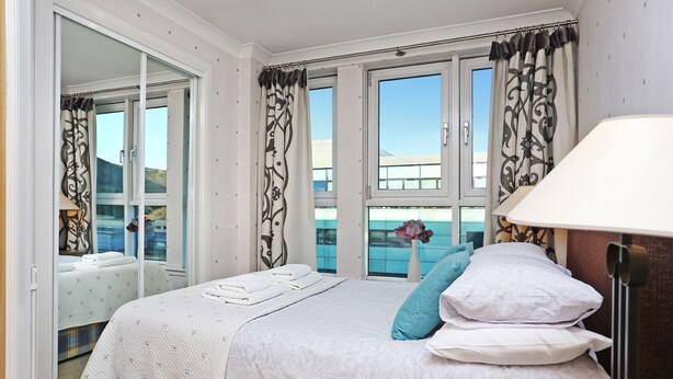 A bedroom with a bed, a nightstand, a lamp, and a window with curtains. - Edinburgh Arthur Seat View Apartment (Edinburgh)