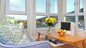A room with a sofa, a table with a chessboard, a vase with flowers, and a bowl of fruit. - Edinburgh Arthur Seat View Apartment (Edinburgh)