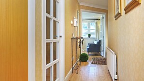 A hallway with a wooden floor, a radiator, a potted plant, and a blue chair in the background. - Edinburgh Arthur Seat View Apartment (Edinburgh)