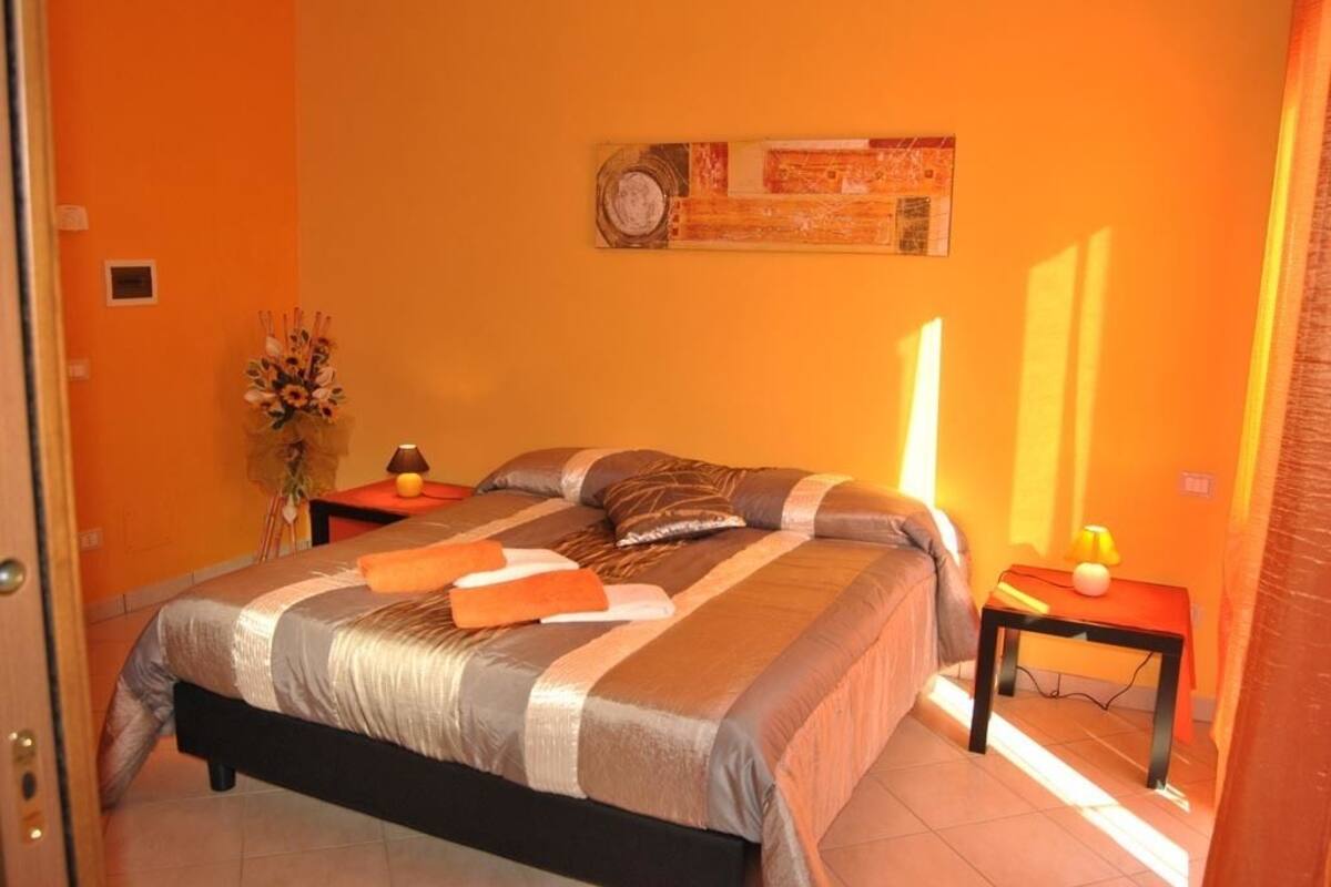Un dormitorio con cama, mesita de noche, lámpara y un adorno en la pared.