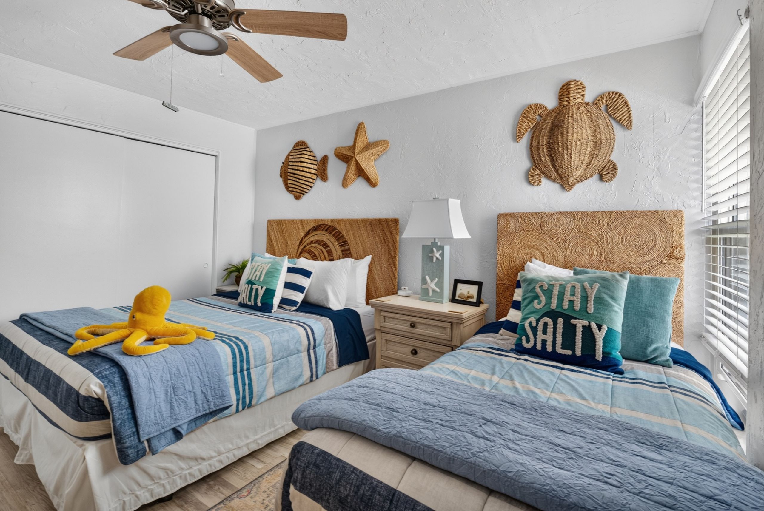 Une chambre avec deux lits, un ventilateur de plafond et des décorations murales comprenant des étoiles de mer et une tortue.