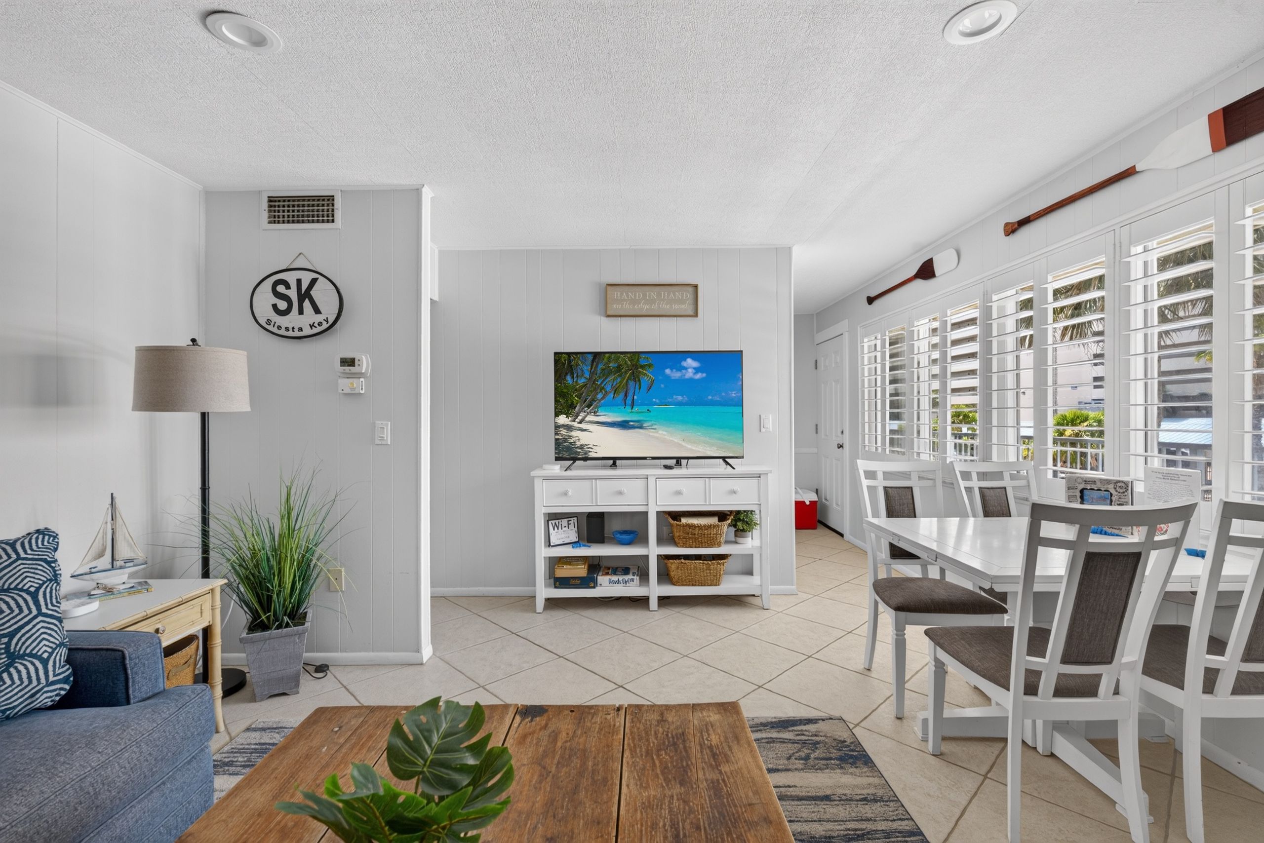 A living room with a TV, a sofa, a coffee table, and a dining area with chairs and a table.