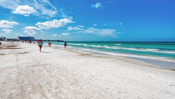 Ein weiter Sandstrand mit blauem Himmel und Meereswellen.
