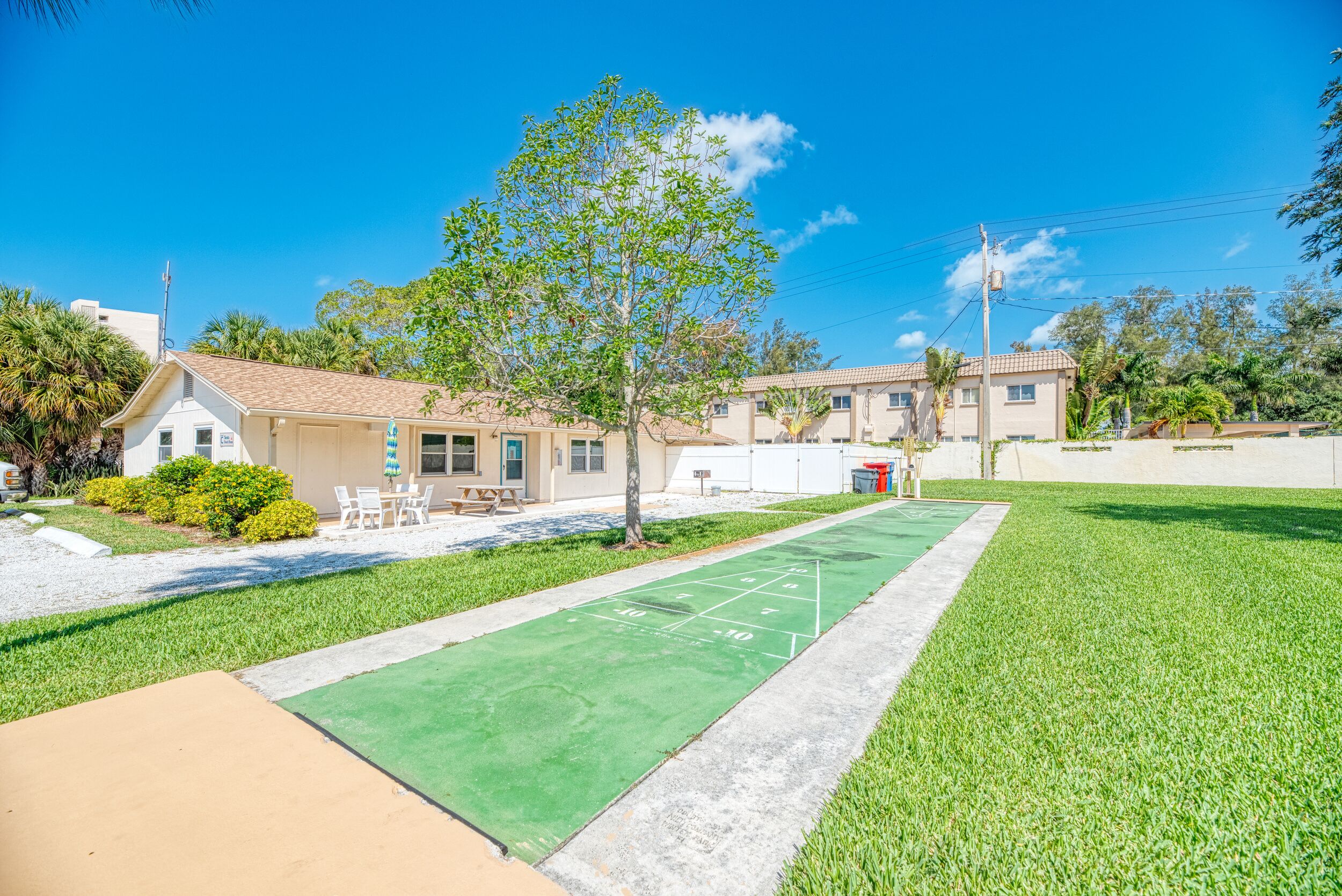Una zona residencial con césped verde, una cancha de shuffleboard y casas con techos color beige.